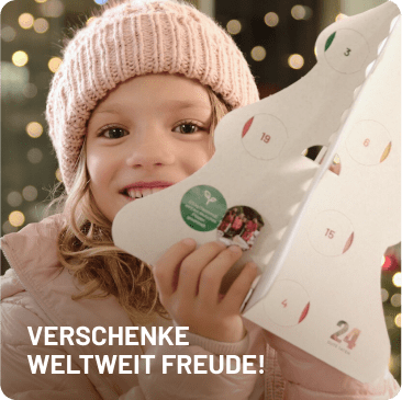 Lächelndes Mädchen mit rosa Mütze hält den 24guteTaten Adventskalender vor weihnachtlicher Kulisse. Text: „Verschenke weltweit Freude!“